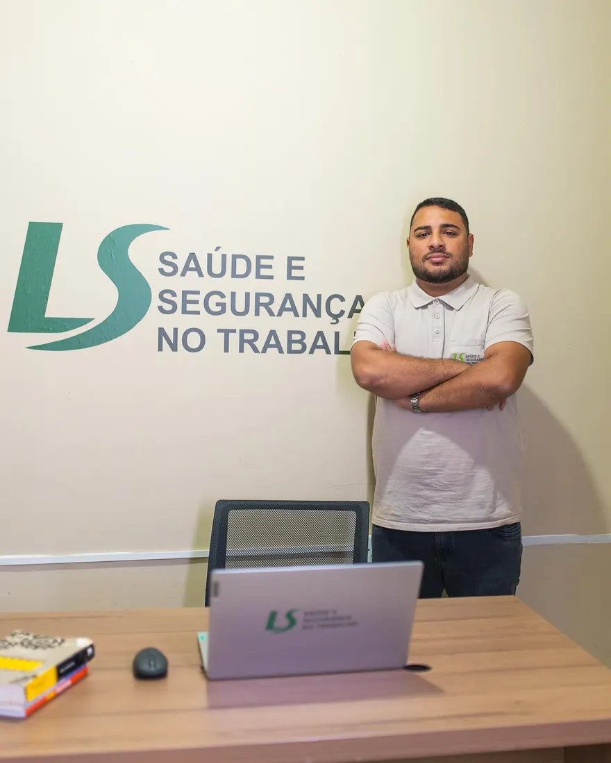Técnico da LS de braços cruzados no escritório, em frente à parede com o logotipo da empresa