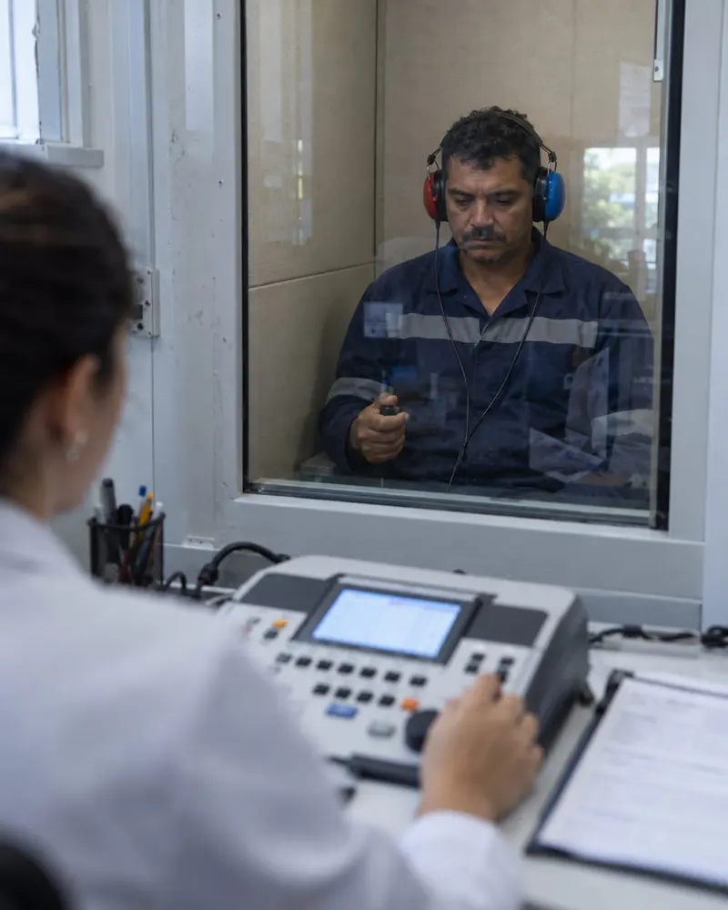 Trabalhador fazendo exame de audiometria dentro de uma cabine acústica