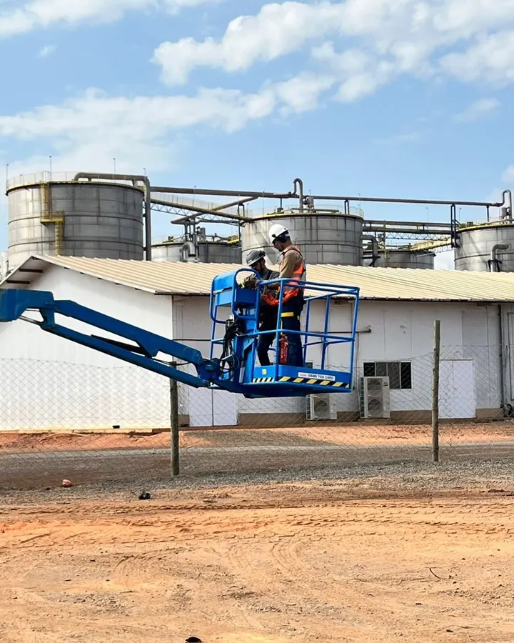 Plataforma elevatória em operação com instrutor e aluno no cesto, em área industrial