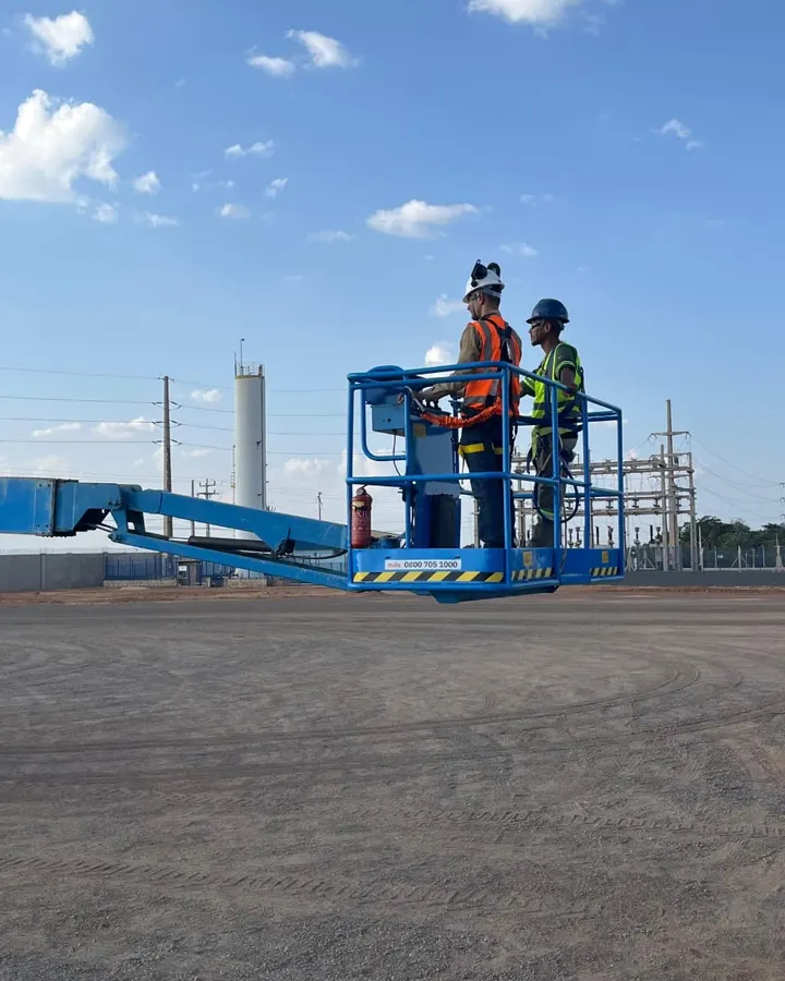Dois trabalhadores com EPI operando uma plataforma elevatória durante treinamento